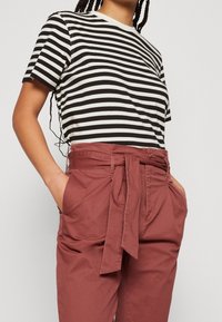 T-shirt à rayures noires et blanches à manches courtes associé à un pantalon taille haute de couleur saumon, doté d'une ceinture à nouer et de poches latérales.