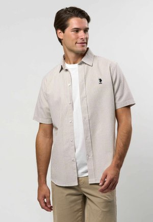 Koszula z krótkim rękawem w kratę w jasnych odcieniach, z zapięciem na guziki i małym, ciemnym logo na piersi. Noszona na białym t-shircie.