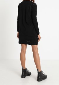 Svart långärmad stickad klänning, rak skärning med rund halsringning, i kombination med svarta ankelstövlar med runda tår och snörningsdesign.