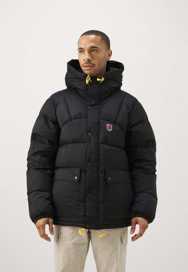 Black, puffy jacket with a high collar and button closure; features yellow drawstrings and two front pockets with flap covers.