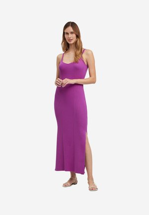 Robe maxi violette à côtes avec des fines bretelles, dotée d'une fente sur le côté. Texture lisse, design ajusté qui met en valeur la silhouette. Accompagnée de sandales à lanières.