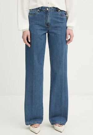 Persona che indossa jeans blu a vita alta con gamba dritta, camicetta bianca a maniche lunghe e tacchi bianchi con punta affilata e fibbia dorata.