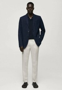 Marinblå blazer, marinblå stickad skjorta, beige byxor och svarta sandaler. Blazern har en enskild bröstficka, skräddarsydd passform och lättviktig tyg.