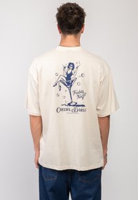 Krémové oversized tričko se námornickou grafikou sedící postavy s koktejlem, obklopené bublinkami, a textem "Páteční noc."