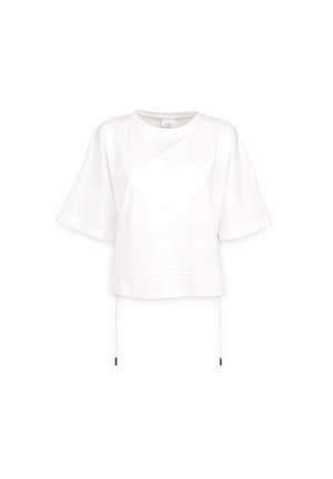 Haut oversize blanc à manches courtes avec encolure ronde et ourlet à cordon avec embouts métalliques, présenté sur fond blanc.