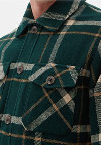 Camicia a quadri verdi con bottoni in misto lana, dotata di tasche, con motivi check beige e bianchi, colletto arrotondato e bottoni scuri.