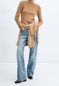 Beżowy sweter prążkowany, oversize, w połączeniu z jasnoniebieskimi spodniami typu wide-leg. Czarne buty na obcasie oraz dopasowany sweter związany w talii.