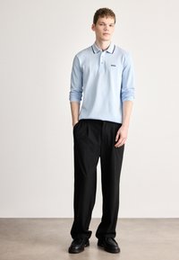 Ανοιχτό μπλε πόλο πουκάμισο με μακριά μανίκια και μαύρο περίγραμμα, με λογότυπο στο στήθος. Συνδυάζεται με μαύρο παντελόνι άνετης εφαρμογής και μαύρα παπούτσια.