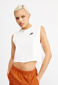 Camiseta sin mangas, corta y blanca, hecha de algodón, con un pequeño logo negro de Nike en el pecho. La camiseta tiene un escote redondo.