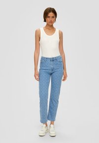 Jean en denim bleu avec un motif de tourbillons bleu clair, taille haute et coupe droite, associé à un débardeur blanc.