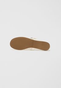 Open-toe sandal with a textured cream-colored upper, adjustable strap, and a brown rubber sole featuring horizontal grooves.