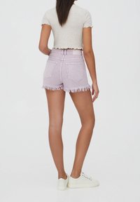 Liliowe szorty dżinsowe z postrzępionym dołem, wysokim stanem i dwoma tylnymi kieszeniami, zestawione z jasno szarym prążkowanym topem o krótkim kroju oraz białymi tenisówkami.