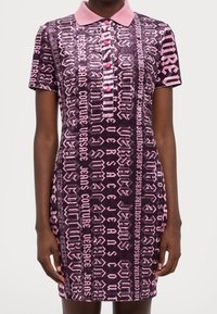 Kratké rukávy polo šaty z měkké, sametové látky. Růžový a tmavě fialový vzor s logy Versace a grafickým designem textu. Límec na čtyři knoflíky.
