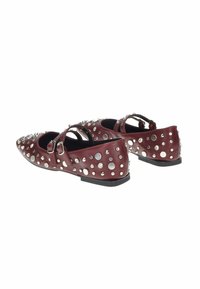 Scarpe flat in pelle di un rosso scuro, con punte affusolate, due cinturini e borchie e decorazioni circolari in argento su tutta la superficie.