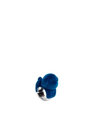 Anillo de terciopelo azul con forma de perro de características redondeadas, soportado por una banda de plata. La superficie presenta una textura suave y un detalle sutil.