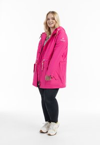 Lys rosa vattentät parkas med huva, dragkedja och tryckknappsstängning, två framfickor, dekorativa snören och en lätt design.