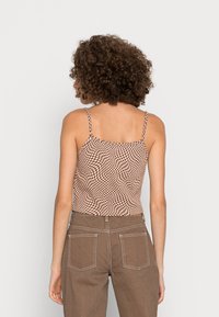 Top cropped em xadrez castanho e creme com alças finas, apresentando um padrão ondulado, combinado com calças castanhas de cintura alta.
