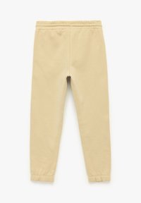 Helle beige Jogginghosen aus weicher Baumwolle mit einem elastischen Bund und gerafften Säumen. Glatte Textur und schlichtes Design.