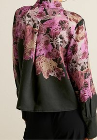 Long-sleeve blouse in black fabric with a floral pattern in pink and gold. Features a collar and a relaxed silhouette. Smooth texture.