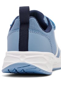 Dos d'une chaussure de sport bleu clair avec languette en tissu bleu foncé et semelle blanche texturée sur fond blanc.