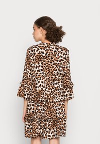 Vestido com padrão de leopardo apresentando um design em camadas, mangas três quartos e detalhes em ruffles em tons de castanho, preto e branco. Textura suave.