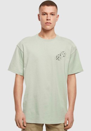 Dæmpet grøn, kortærmet t-shirt i bomuld. Har et trykt design af to terninger på venstre bryst. Løs pasform og rund halsudskæring.