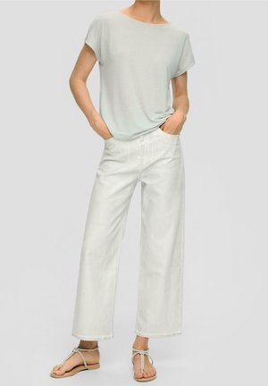 T-shirt à manches courtes gris clair associé à un jean blanc taille haute à jambes larges. Sandales beiges à lanières avec une semelle plate. Tenue décontractée.