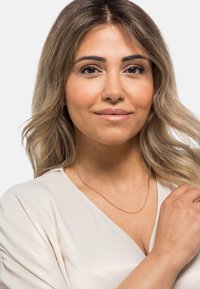 Collana a catena in oro rosa su una donna, caratterizzata da un design delicato, un aspetto stratificato e una texture liscia, indossata sopra un top chiaro.