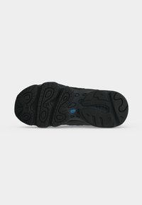 Μαύρη σόλα αθλητικού παπουτσιού New Balance με ανάγλυφα ελαστικά μοτίβα και ορατό όνομα επωνυμίας στην περιοχή της φτέρνας σε απλό φόντο.