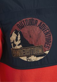 Donkere jas met een cirkelvormige bergafbeelding en de tekst "BUITENAVONTUREN" en een gestikt "VANDERSTORM" patch.
