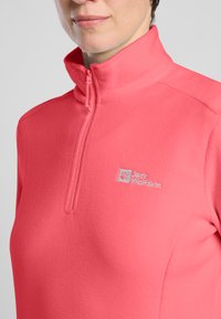 Pullover in pile di colore rosa brillante, con colletto a mezza zip e un piccolo logo sulla parte sinistra del petto. Materiale testurizzato e leggero.