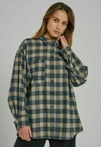 Rutig oversized skjorta i beige och mörkblå, tillverkad av mjukt tyg. Har knappstängning, spetskrage och långa, puffiga ärmar.