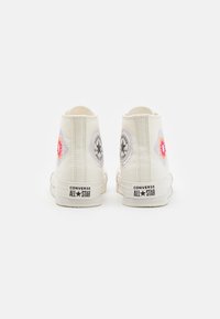 Zapatillas altas de lona blanca con diseños florales bordados en ambos lados y la marca "Converse All Star" en negro en el talón.