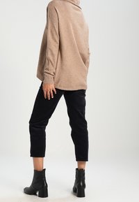 Beige oversized trui met col, gecombineerd met marineblauwe corduroy cropped broek en zwarte enkellaarsjes met hak. Soepele textuur, ontspannen pasvorm.