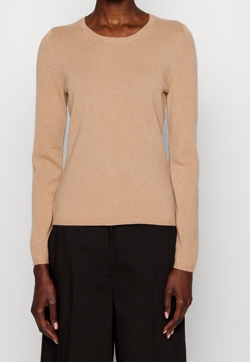 Hellbeige Langarmpullover mit Rundhalsausschnitt, weicher Textur, gerippten Details an den Bündchen und dem Saum, kombiniert mit schwarzer weiter Hose.