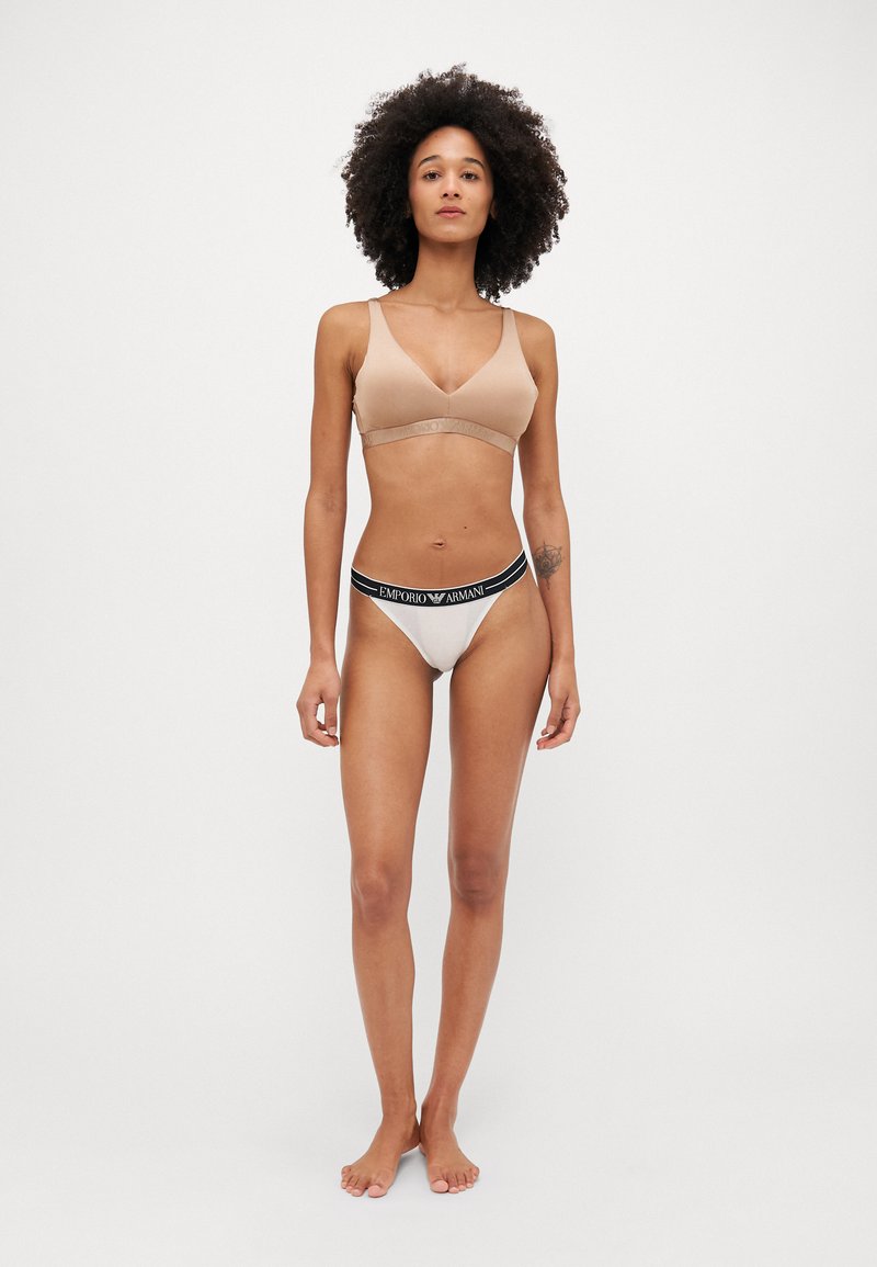 Bralette sans fil beige avec des fines bretelles et une bande texturée ; string crème assorti avec une ceinture logo noire.