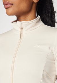 Helle beige Zip-Jacke mit hohem Kragen, weichem Stoff und athletic Schnitt. Verfügt über dezente Logodetails und genähte Akzente.