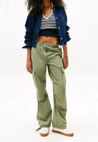 Tikkihame tummansinisestä denimista, lyhyt raidallinen tummansininen ja valkoinen toppi, oliivinvihreät cargo-housut sivutaskuilla, ja valkoiset lenkkarit ruskeilla pohjilla.