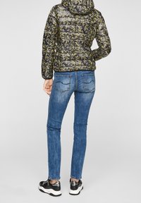 Sort og gul blomsterpufferjakke med hætte, parret med blå skinny jeans og sorte sneakers med sølvdetaljer.