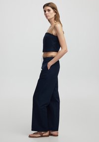 Haut court bleu marine en tissu lisse, associé à un pantalon large bleu marine avec poches et taille à cordon.
