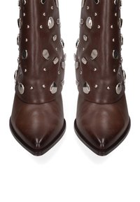 Een paar donkerbruine leren laarzen met spitse neuzen, bezaaid met verhoogde zilveren studs aan de voorkant en zijkanten.