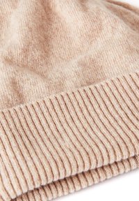 Cappello lavorato a maglia beige con bordino a coste, texture morbida e una finitura leggermente pelosa, caratterizzato da una palette di colori caldi e tenui.