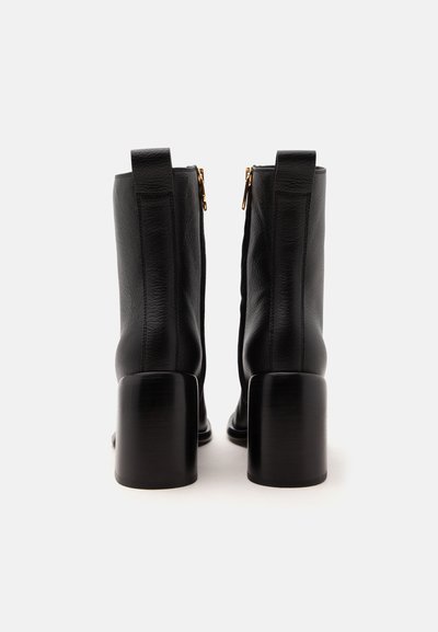 Paire de bottines en cuir noir avec talons blocs et fermetures éclair latérales, vues de dos sur fond blanc.