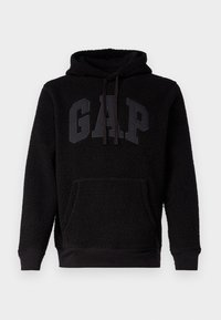 Schwarzer, flauschiger Kapuzenpullover mit vorderer Kängurutasche und großem GAP-Logo in erhabenen schwarzen Buchstaben über der Brust.