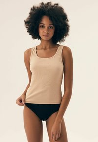 Beżowy prążkowany top na ramiączkach z kwadratowym dekoltem, w połączeniu z czarnymi spodniami z wysokim stanem. Materiał wydaje się miękki i ma dopasowany krój.