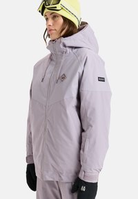 Paarse sneeuwjas met ritssluiting, capuchon en subtiel ruitpatroon. Heeft een "ROXY" label en zwarte handschoenen, geschikt voor wintersport.