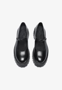 Black leather Mary Jane shoes with a round toe, a single strap, and a thick, rugged sole featuring textured accents.