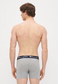 Boxers en coton gris avec une taille élastique marine arborant le logo "Champion". La vue de dos montre un design ajusté.