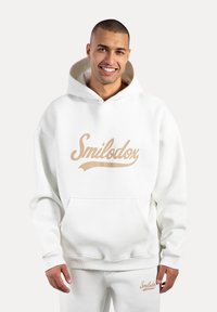 Sudadera blanca con un gran logo "Smilodox" en color beige. Presenta un bolsillo canguro, puños acanalados y una capucha forrada. Material suave y aterciopelado.