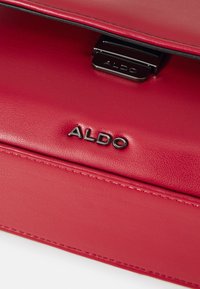 Raudona odinė rankinė su lygiu paviršiumi, stačiakampiu pavidalu ir metaliniu užsegimu. ALDO logotipas išraižytas priekyje.